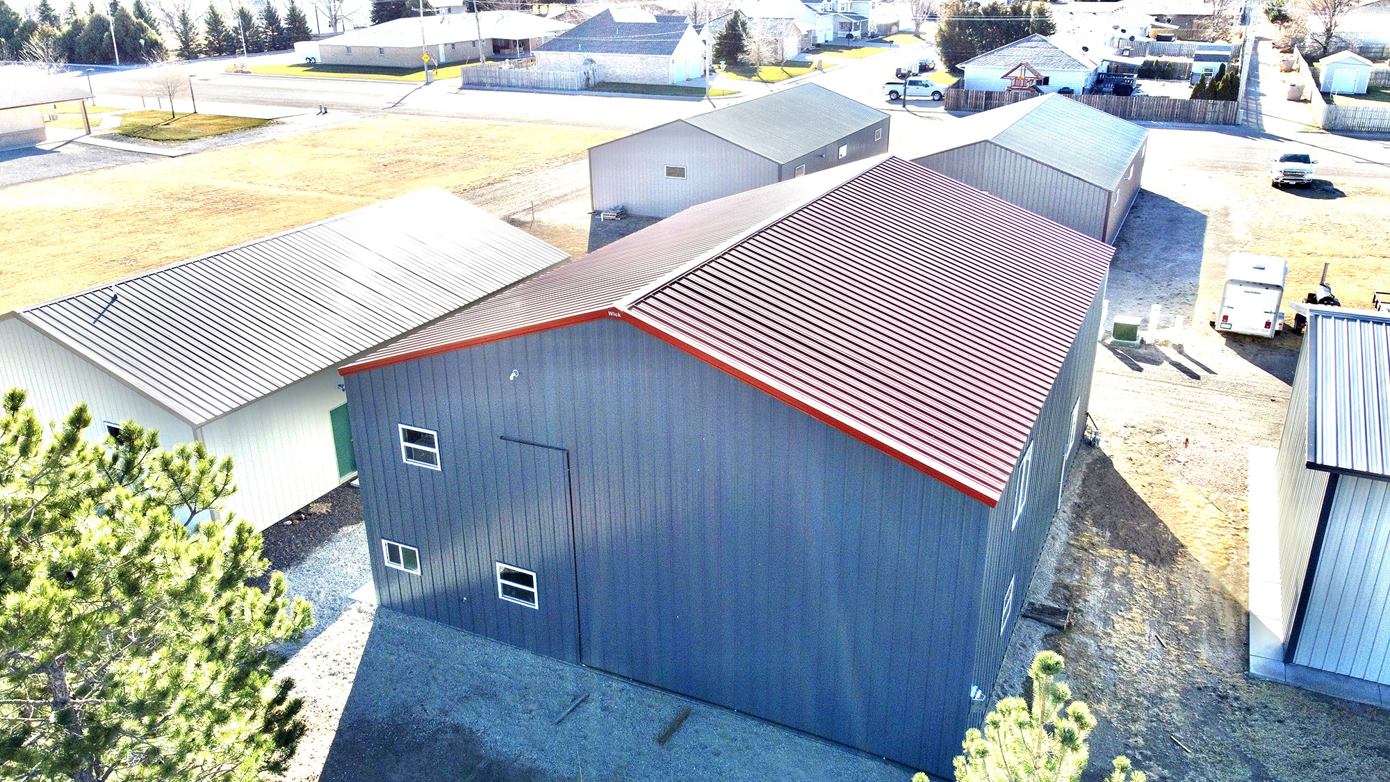 gray post frame suburban building with a red roof and white doors and garage doord